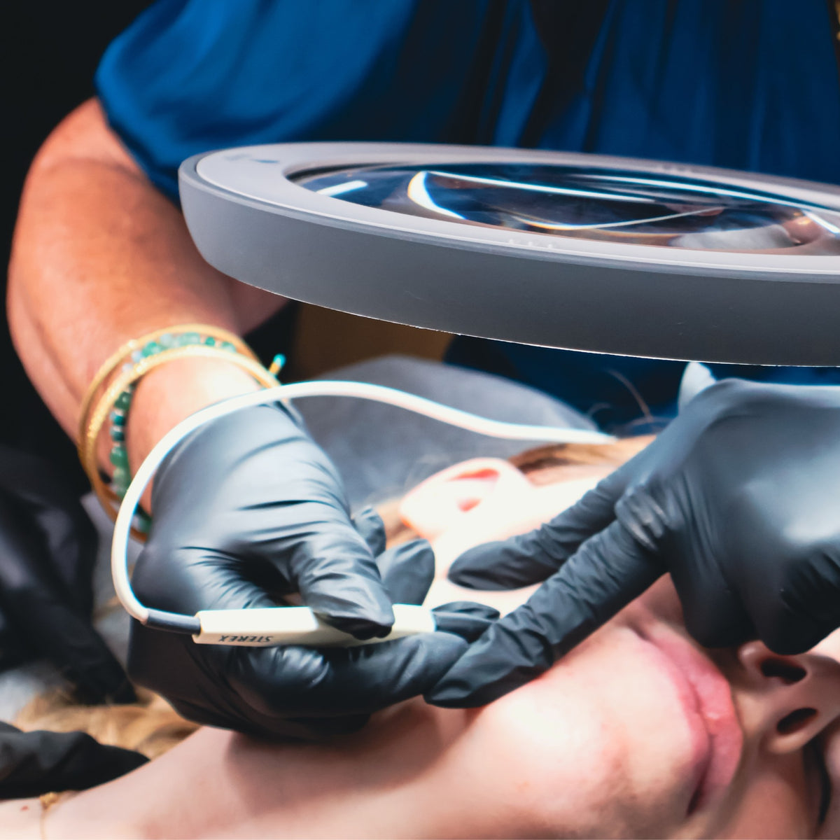 Electrologist using a Sterex probe under a magnifying lamp during SHBBHRS013 electrolysis training